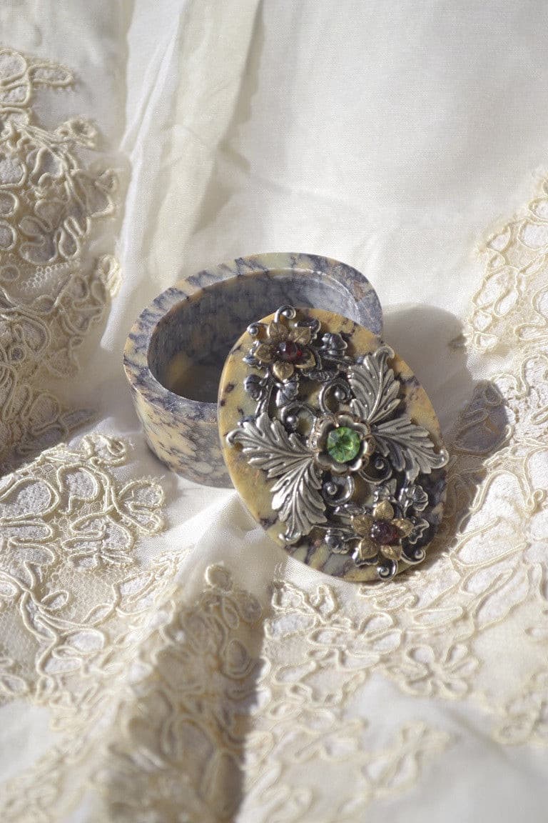 Jeweled oval soapstone keepsake box with green gem and silver floral design on lace fabric