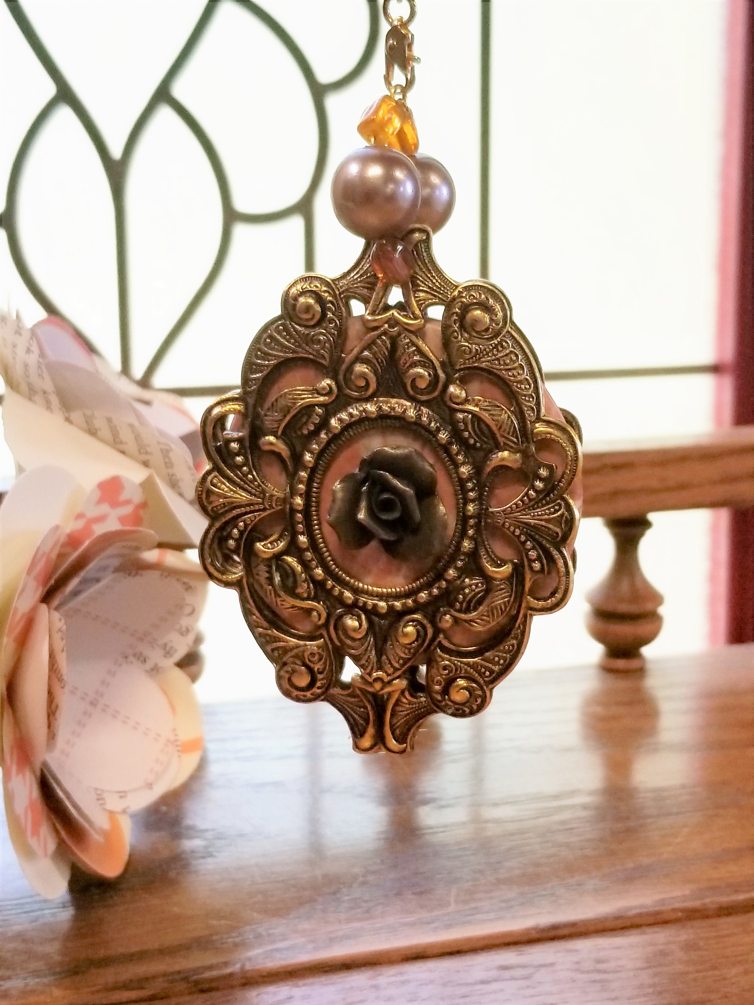 Ornate gold pendant with black rose center and pearl accents, hanging in natural light