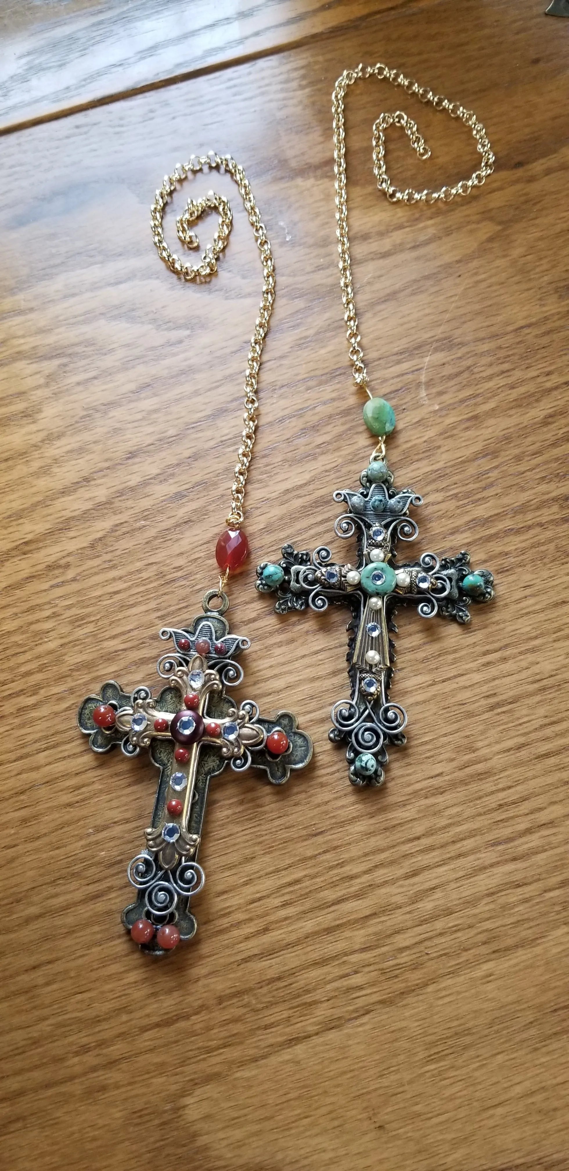 Jeweled ornate cross necklaces with gold chains on wooden surface, featuring gemstones and filigree.