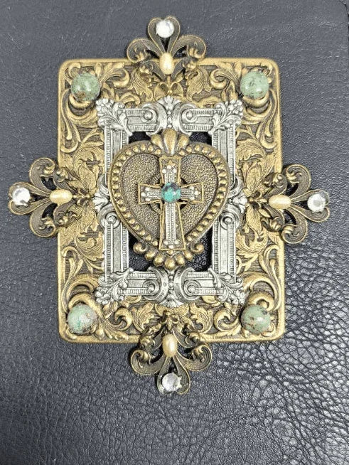 Handcrafted ornate cross with jeweled heart centerpiece on embossed metal background