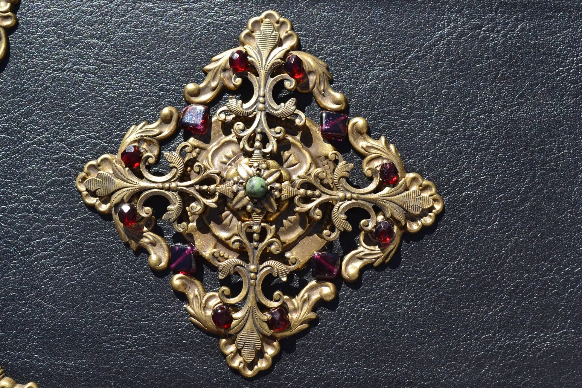 Ornate gold filigree cross with red gemstones on black leather background