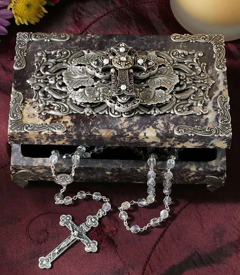 Ornate keepsake box with silver cross and decorative rosary on burgundy fabric background