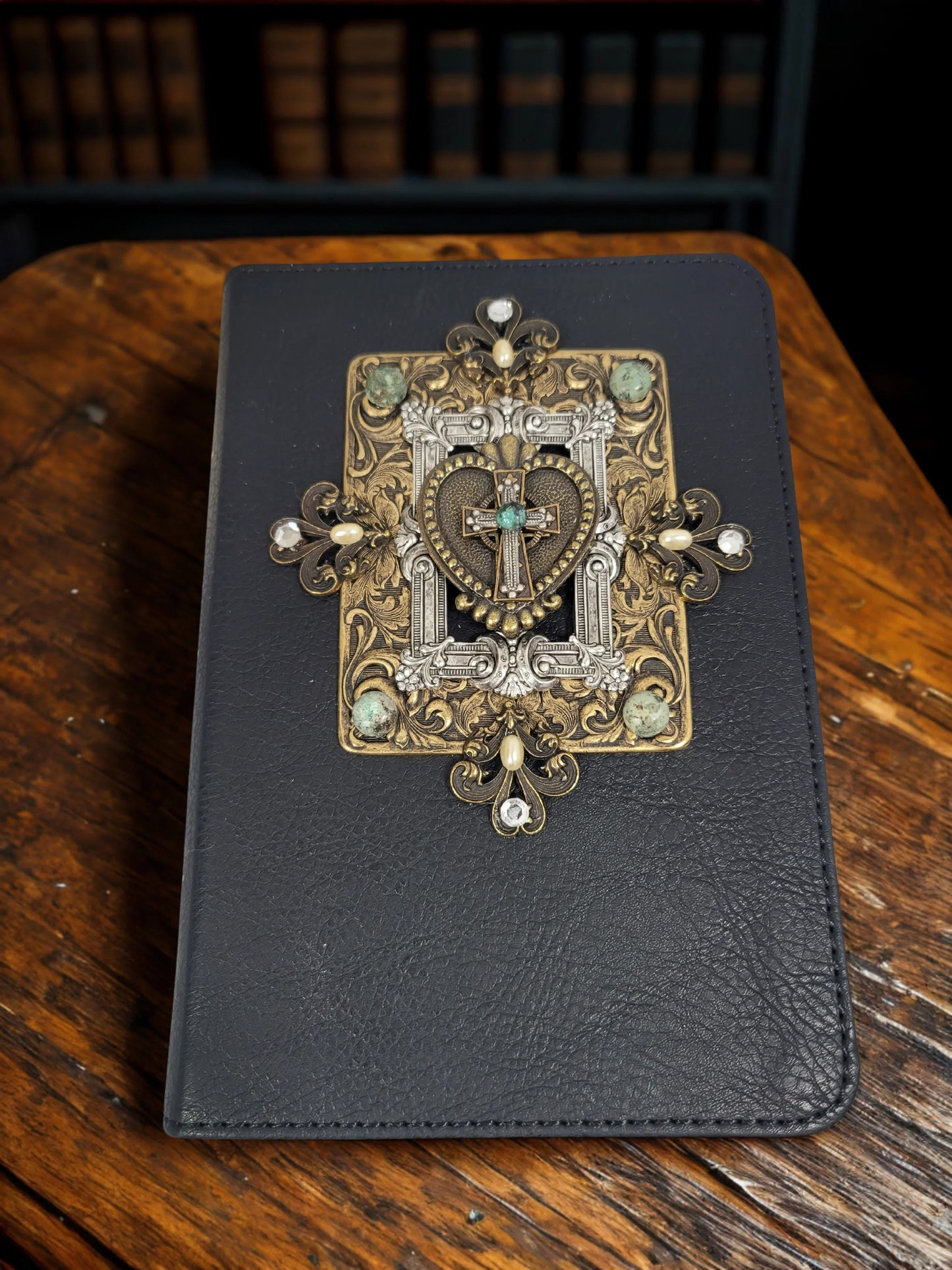 Jeweled Bible with ornate cross and heart design on black leather cover, resting on wooden desk