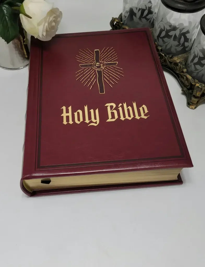 Heirloom Holy Bible with maroon cover, gold cross emblem, and gilded page edges on table