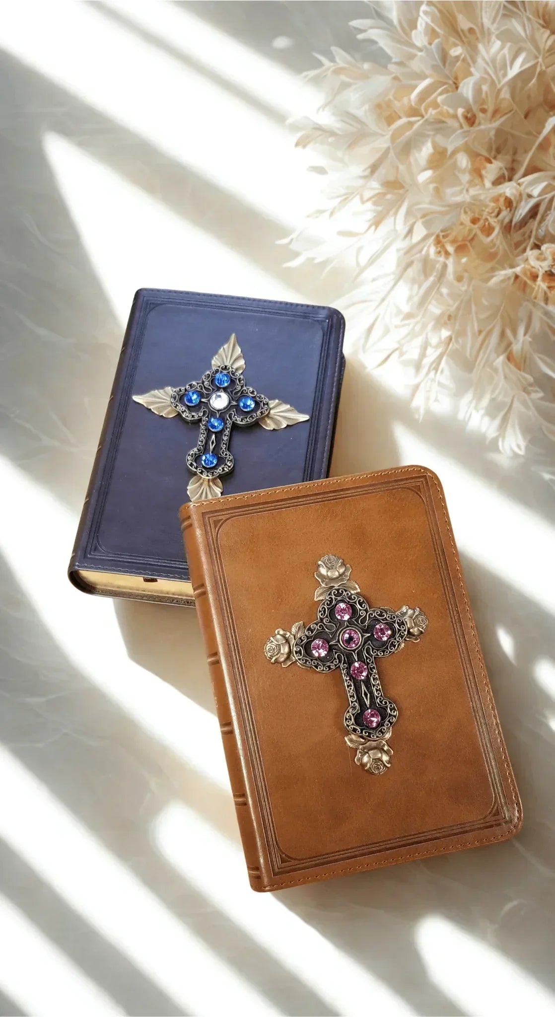 Two jeweled leather Bibles with ornate crosses, one blue and one brown, on a marble surface.