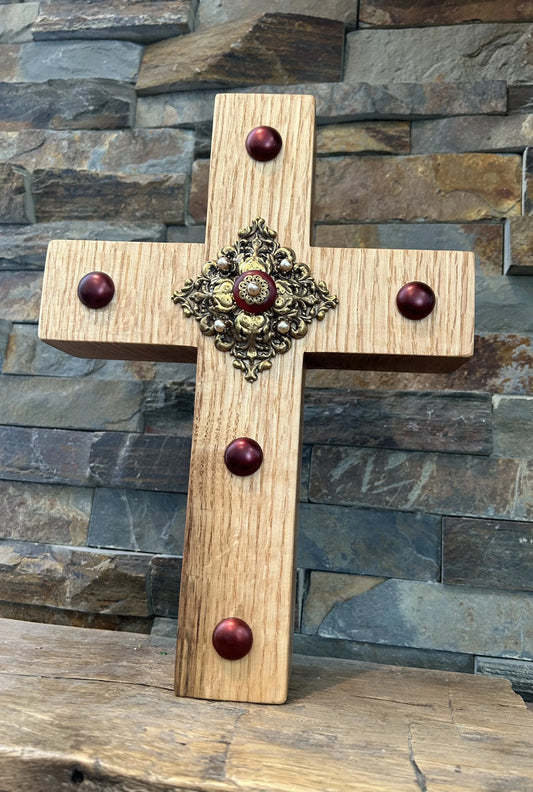 Handcrafted oak wood cross with ornate metal center and red beads, rustic background