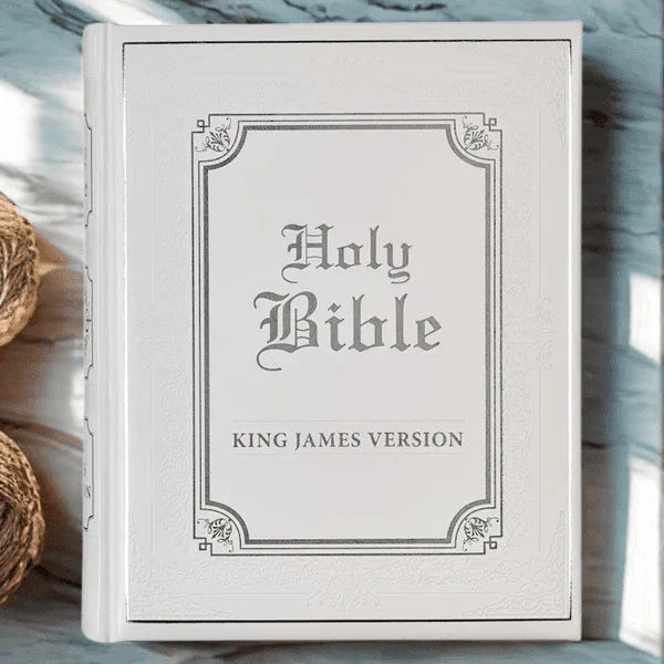 White faux leather King James Bible with ornate silver lettering on light wood surface