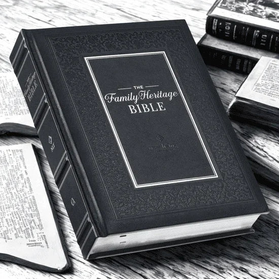 Black hardcover Family Heritage Bible on desk with open books nearby