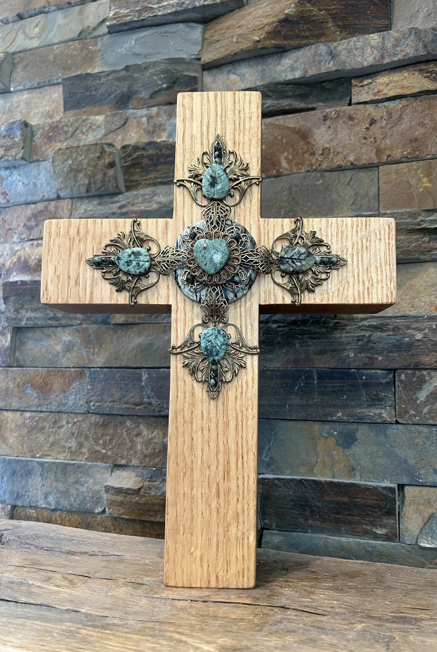 Handcrafted wooden cross with ornate filigree and turquoise stone accents against stone wall