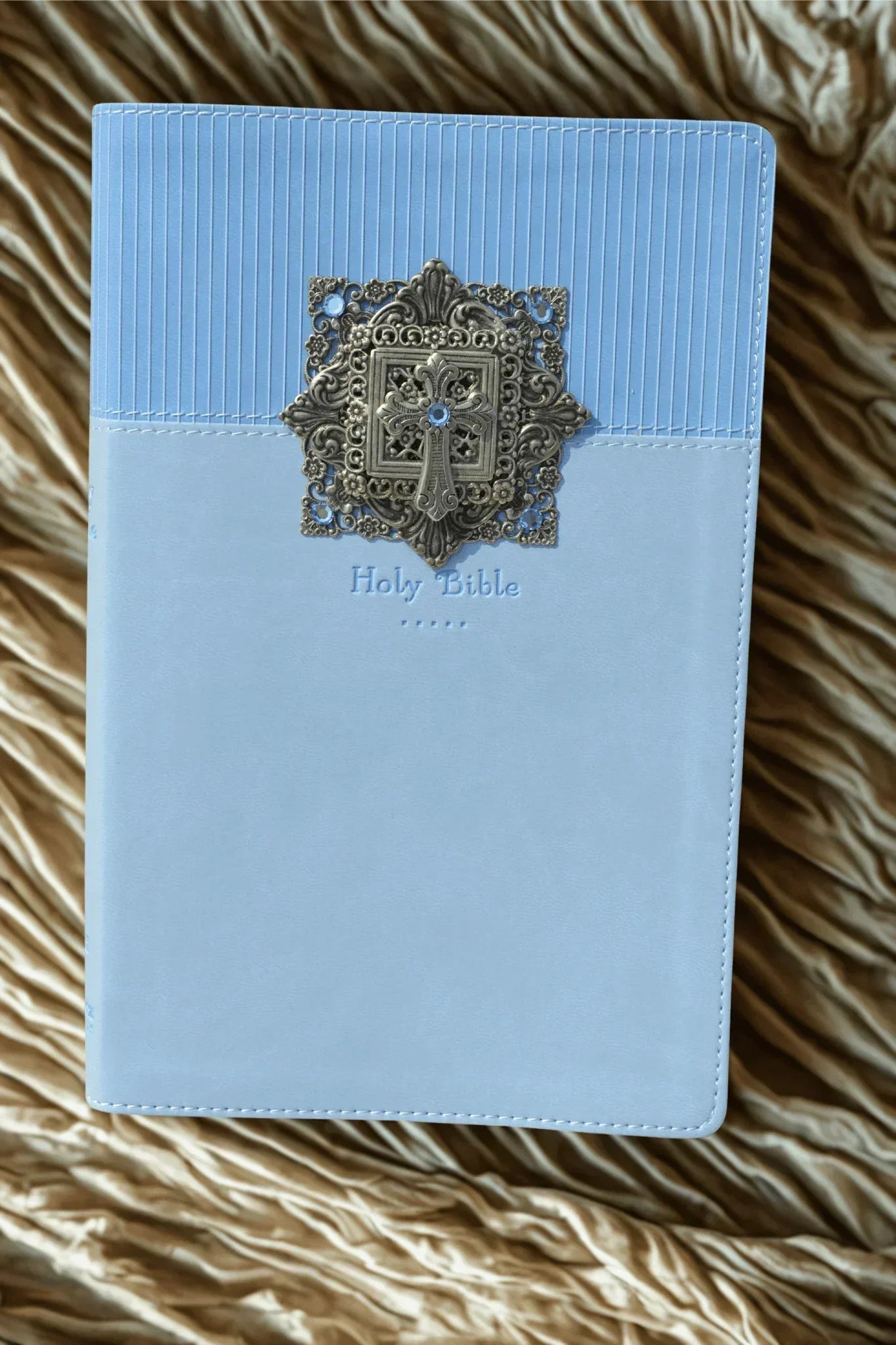 Jeweled baby keepsake Bible with blue cover and ornate metal cross on textured fabric background