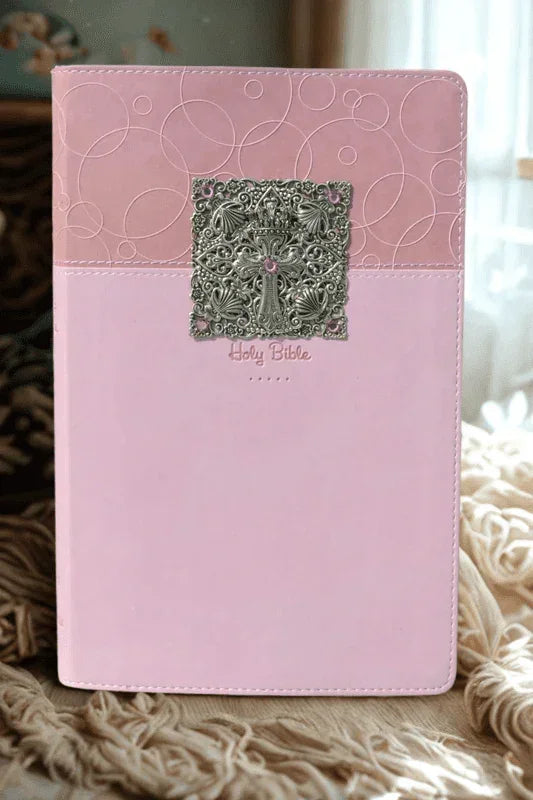 Pink jeweled baby keepsake Bible with ornate silver cross and embossed cover in soft lighting