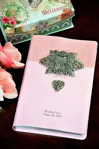 Jeweled pink baby keepsake Bible with ornate metal cross and heart on embossed cover.