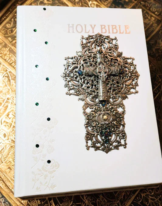 Jeweled white wedding Bible with ornate silver cross and blue gemstones on gold background