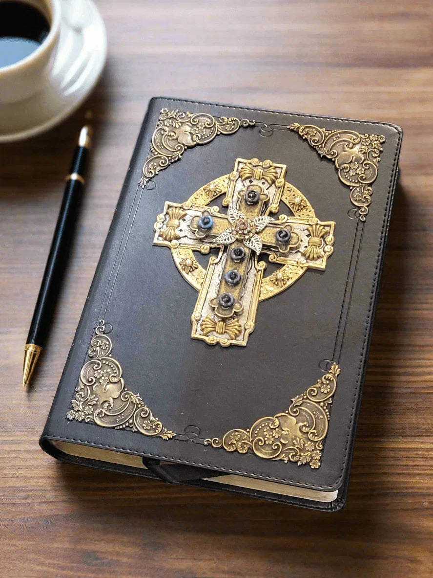 Jeweled Celtic cross Bible with ornate gold accents on black cover, pen, and coffee on desk