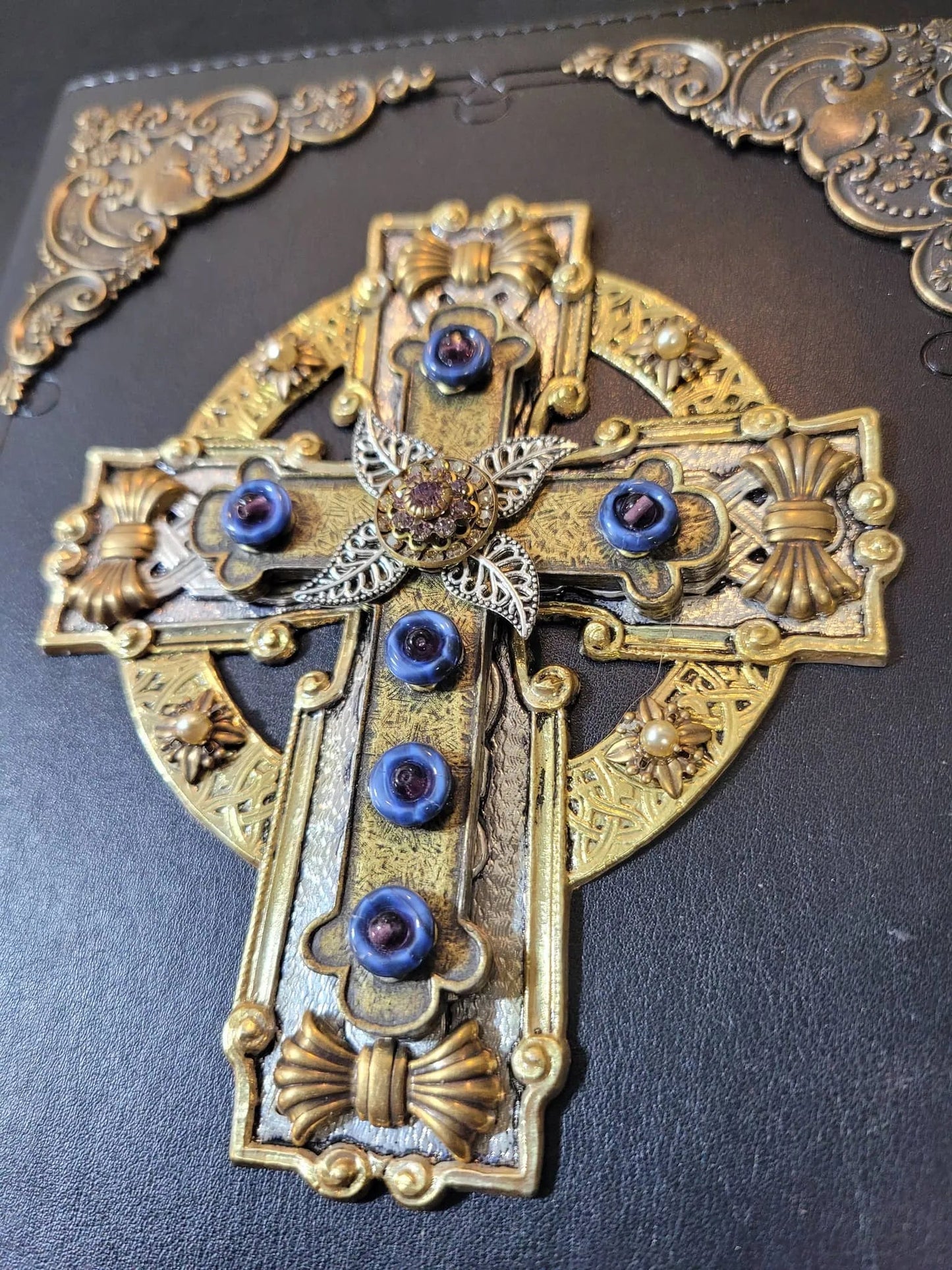 Jeweled Celtic cross with blue gemstones and ornate gold detailing on a black Bible cover