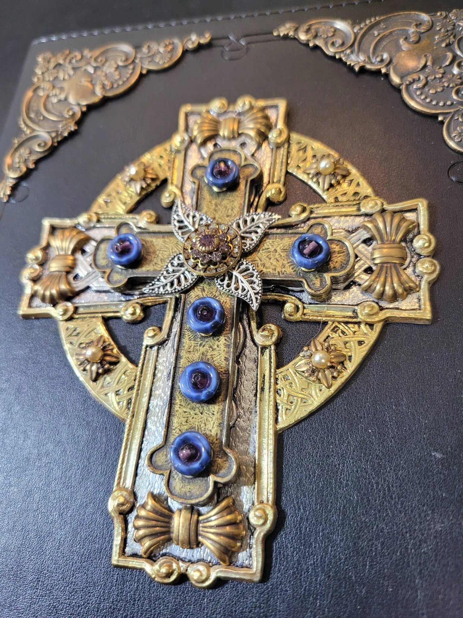 Jeweled Celtic cross with blue gemstones and ornate gold detailing on a black Bible cover