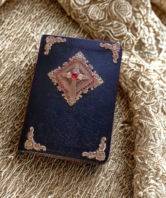 Jeweled black Bible with gold embellishments and red stone centerpiece on ornate fabric