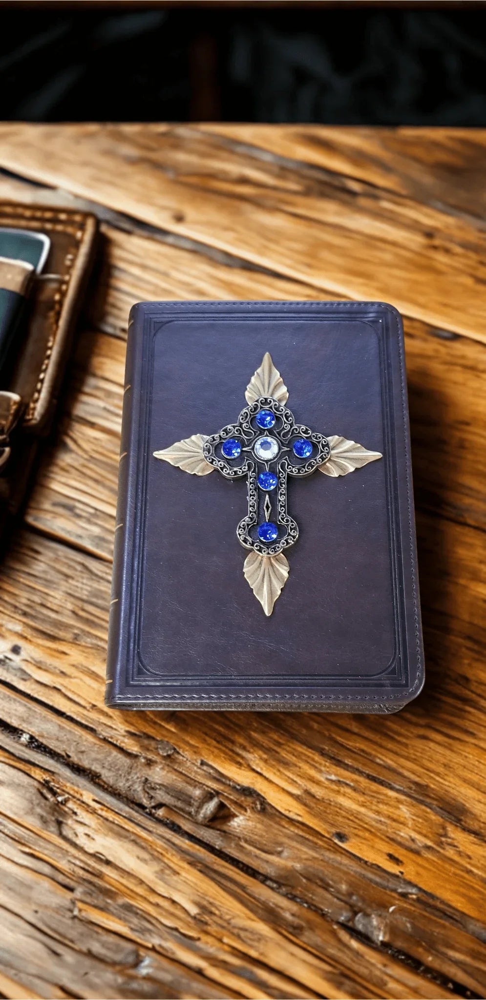 Elegant leather Bible cover with ornate cross and blue gemstones on rustic wood