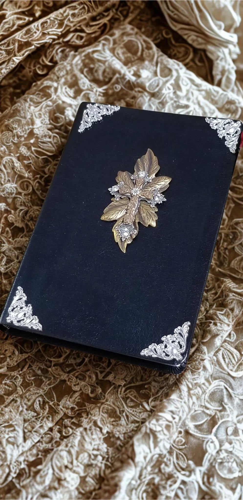 Jeweled black Bible with ornate gold leaf cross and silver filigree corners on lace fabric