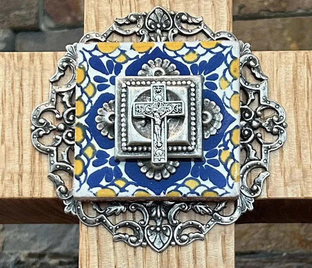 Close-up of a decorative metal cross with blue and yellow floral accents on a wooden background