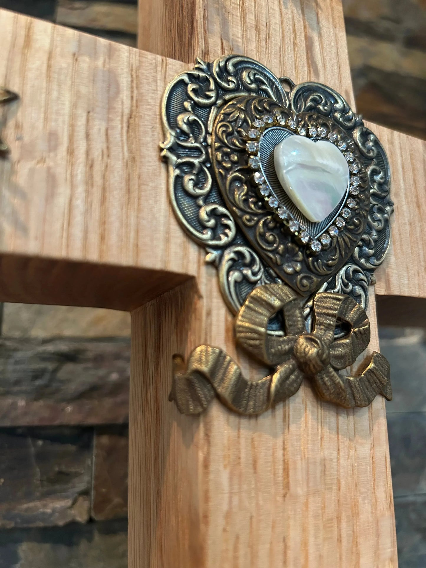Close-up of wooden cross with ornate metallic heart and bow accent, jeweled trim