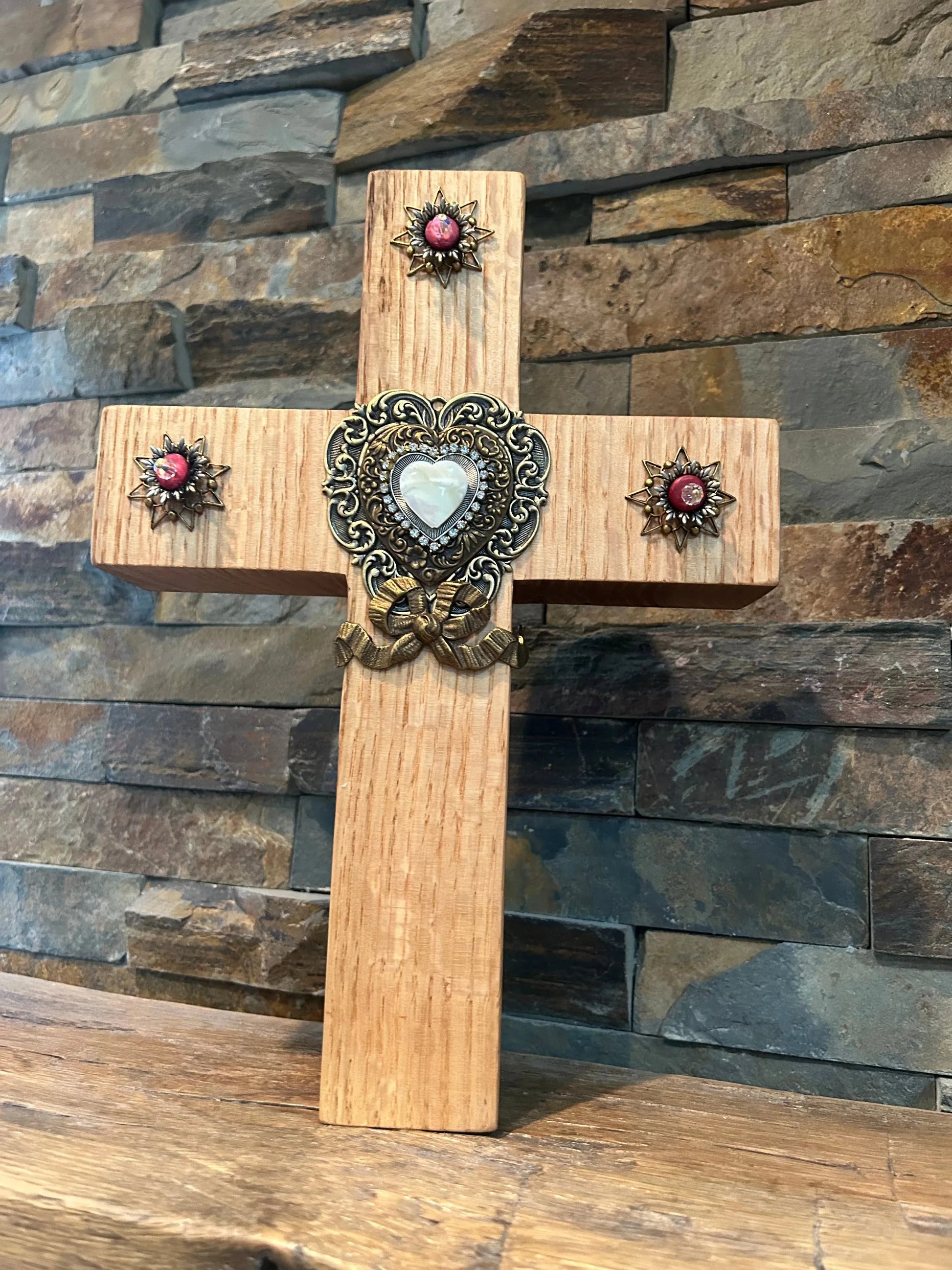 Handcrafted oak cross with ornate pink and white jewels, displayed on a stone background