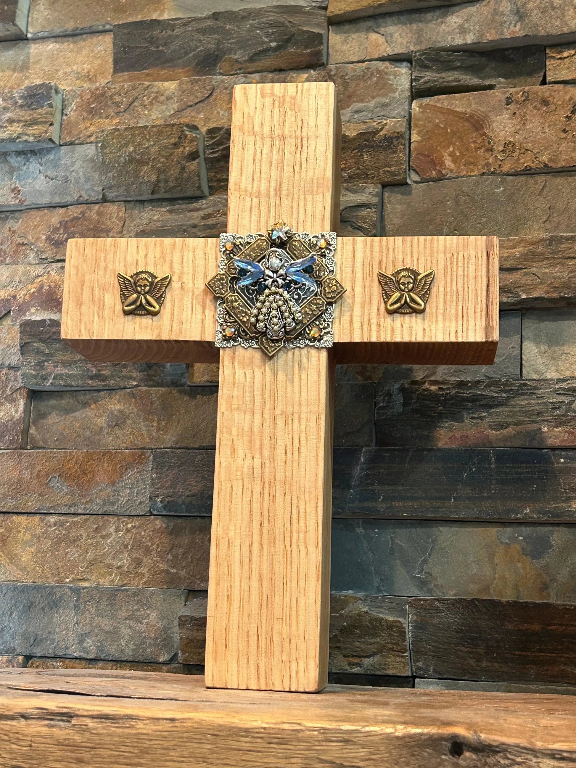 Handcrafted oak cross with jeweled center and angel accents on rustic stone background