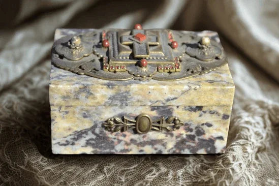Jeweled soapstone keepsake box with ornate cross design on lid, resting on dark fabric.