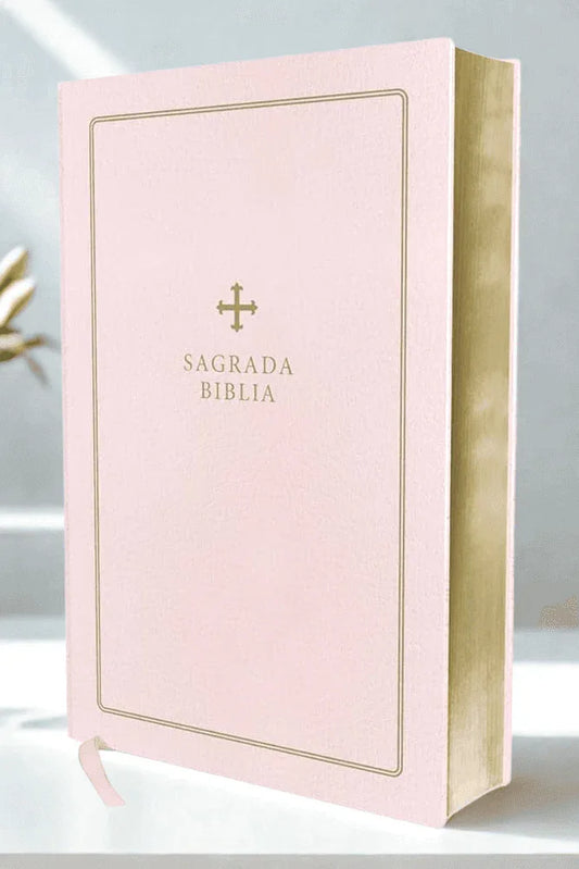 Pink leather Spanish Bible with gold-edged pages and gold cross detail, upright on table.