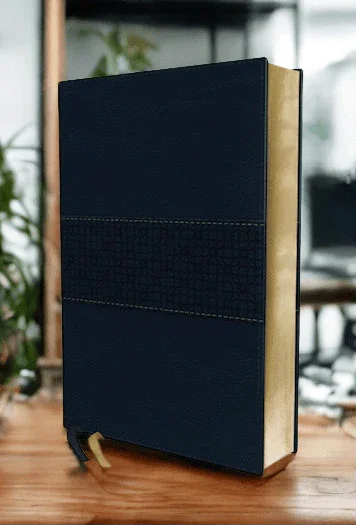 Navy leather Bible with gold-edged pages standing upright on a wooden table