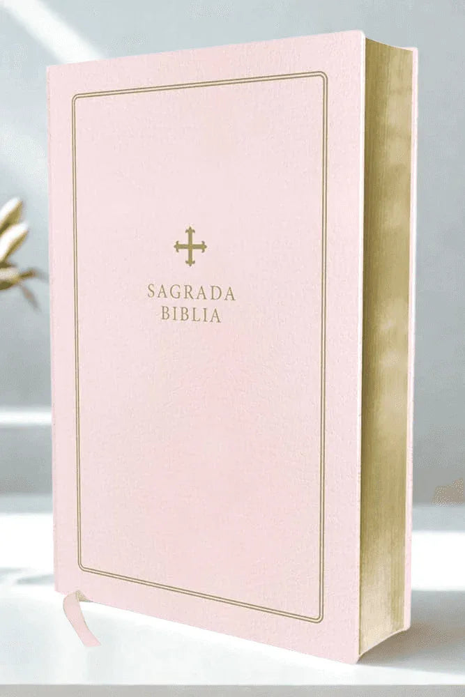 Pink leather Spanish Bible with gold-edged pages and gold cross detail, upright on table.