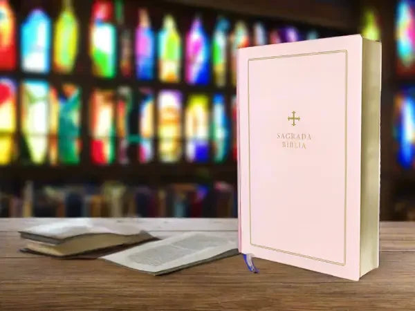 Pink Catholic Bible with gold cross on wooden table, stained glass background, inspirational gift