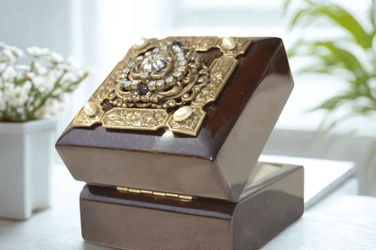 Purple heart wood keepsake box with ornate gold and jeweled lid, open on shiny surface.