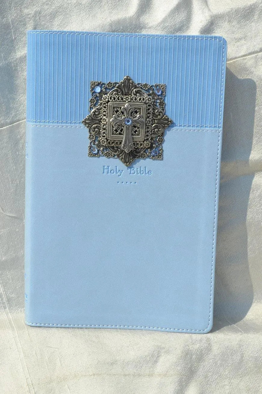 Light blue Holy Bible with ornate silver cross embellishment on cover, displayed on fabric.