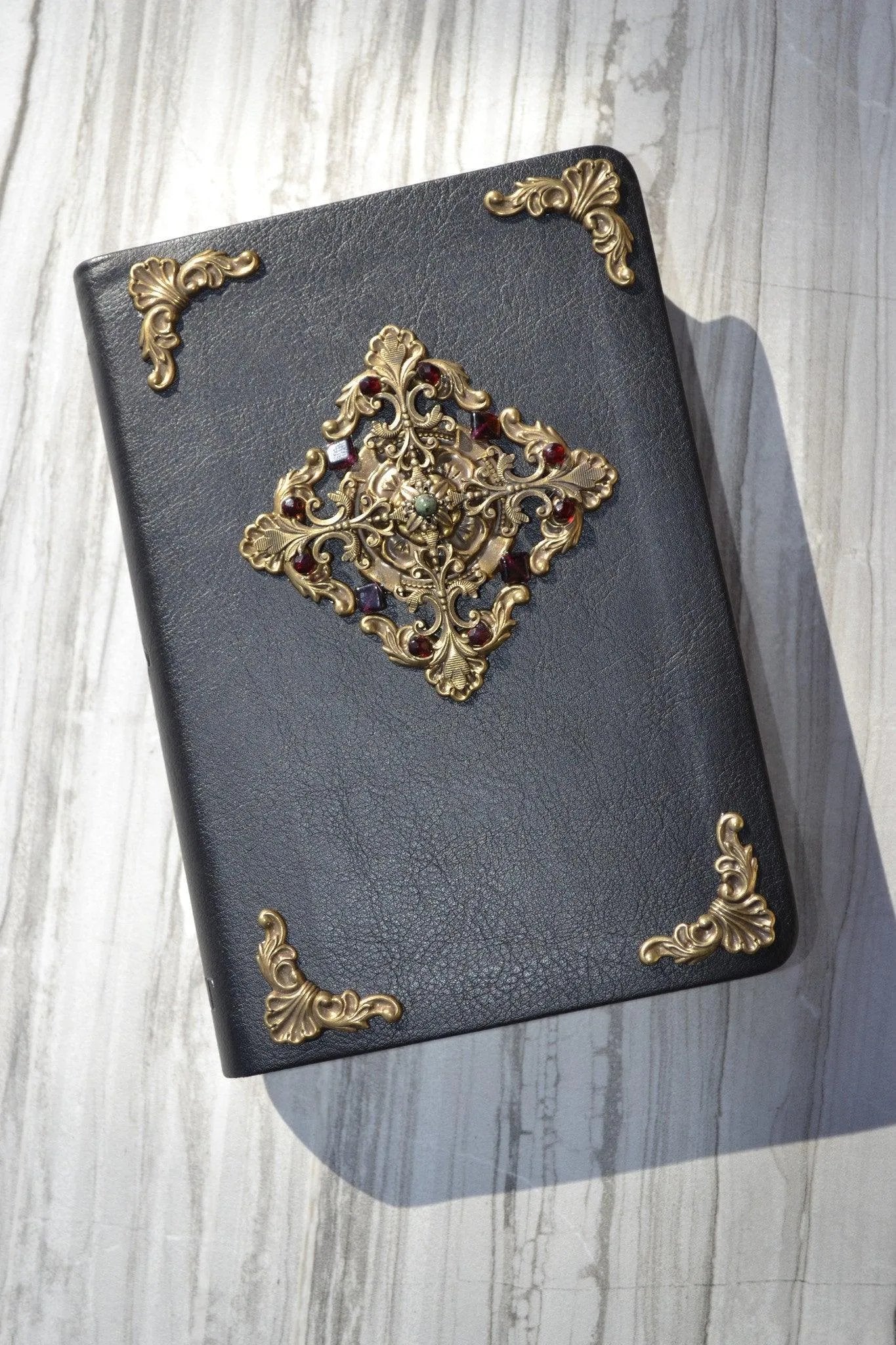 Black leather Bible with ornate gold and jewel embellishments on marble surface