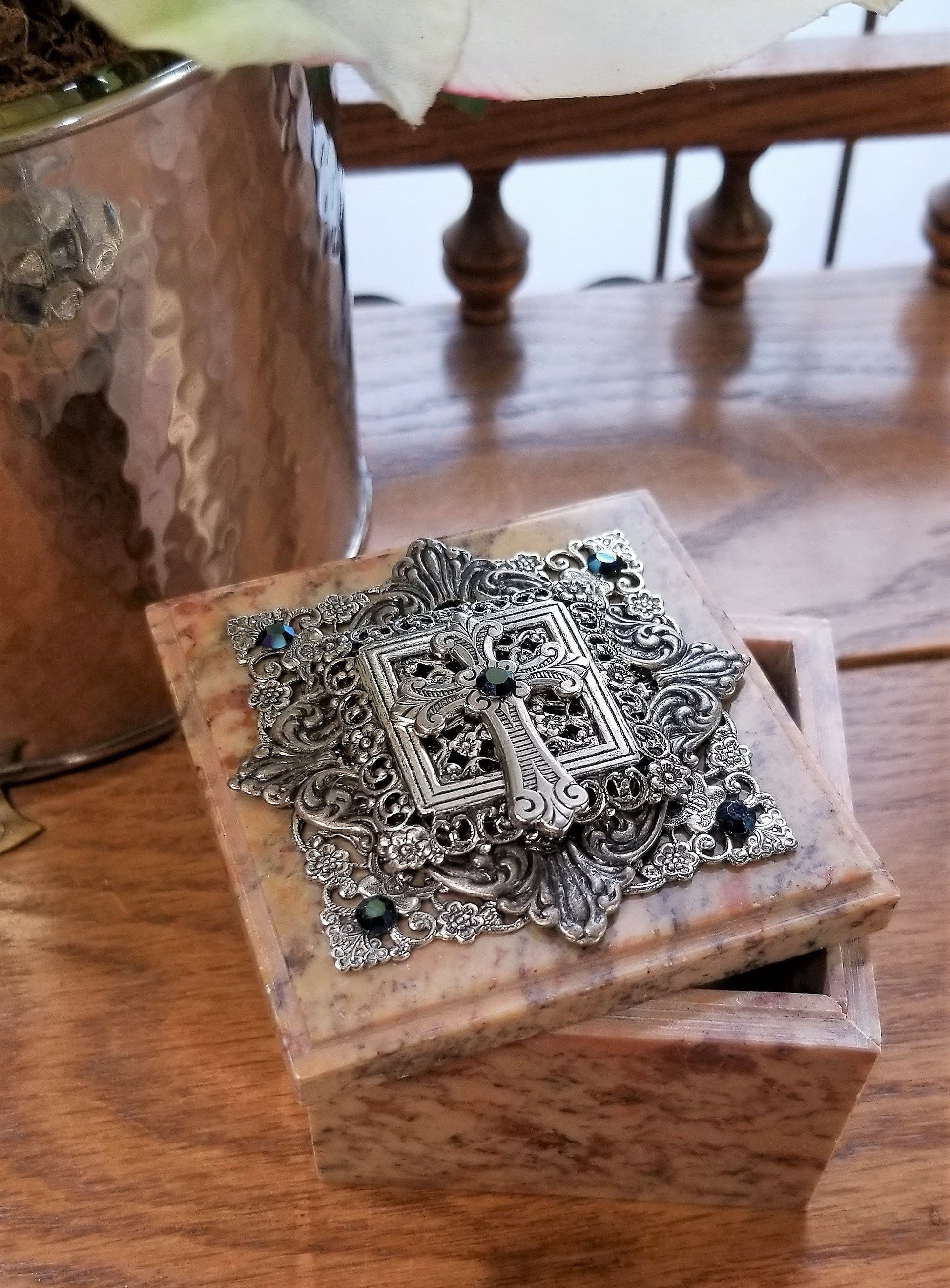 Marble keepsake box with ornate silver cross lid, decorative gemstones, open on wooden table