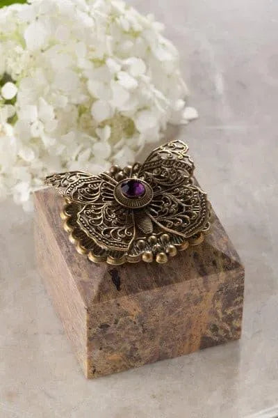 Jeweled butterfly trinket box with ornate metal details and a purple gemstone on a marble surface
