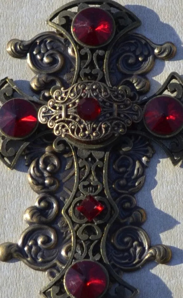 Close-up of ornate antique-inspired cross with intricate detailing and red gemstones