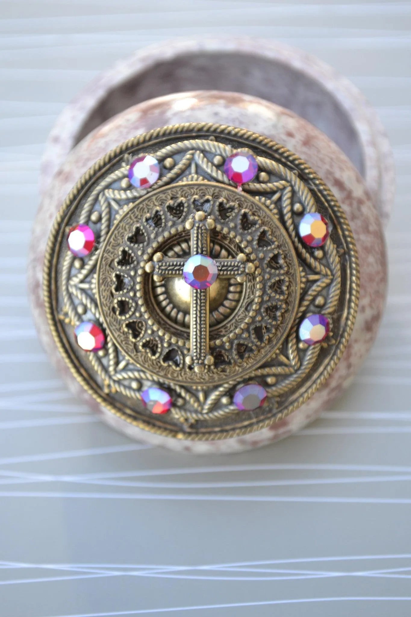 Open round keepsake box with ornate jeweled cross lid and iridescent crystal accents