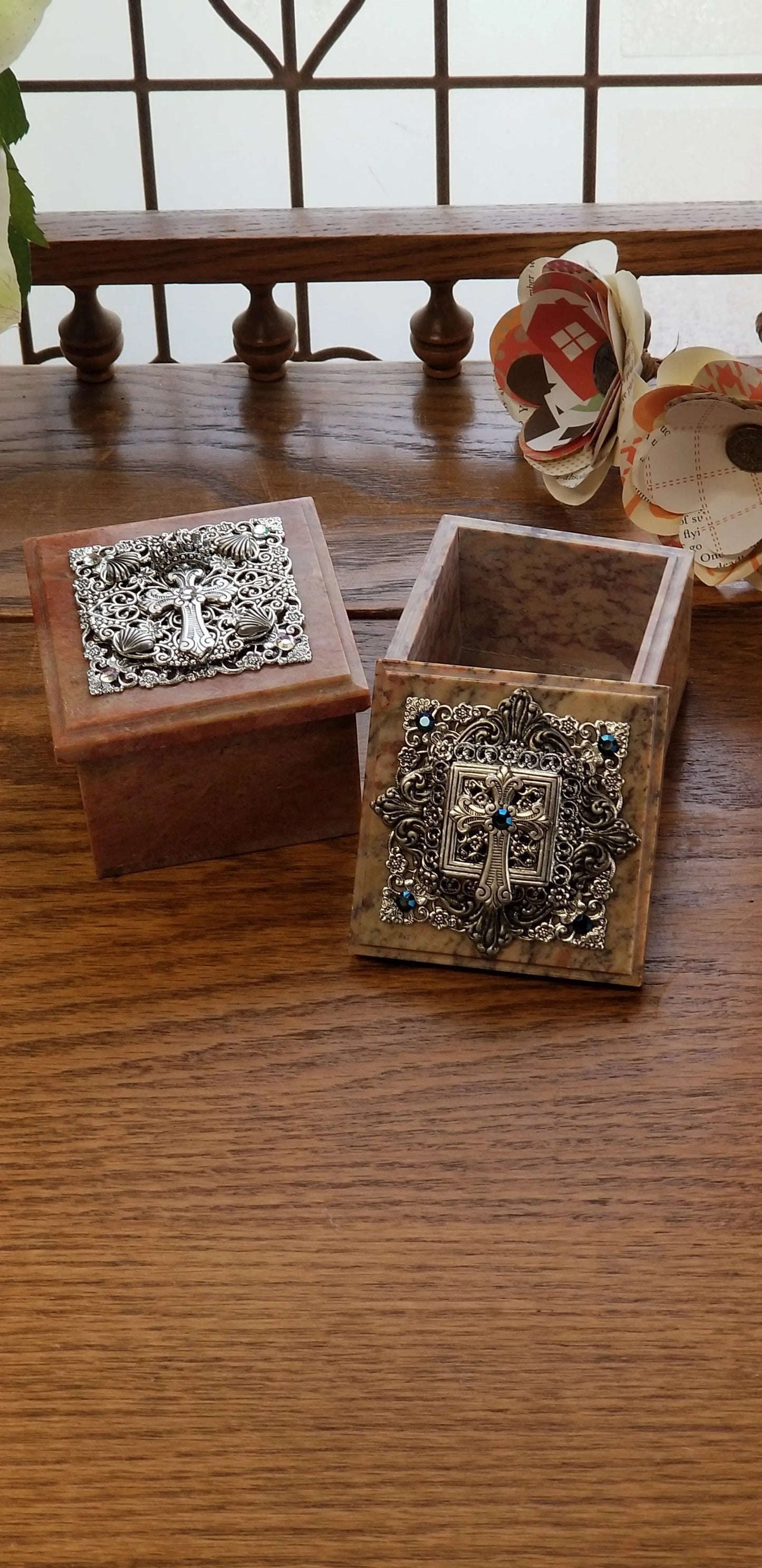 Two ornate keepsake boxes with silver cross and blue gemstone accents on wooden table