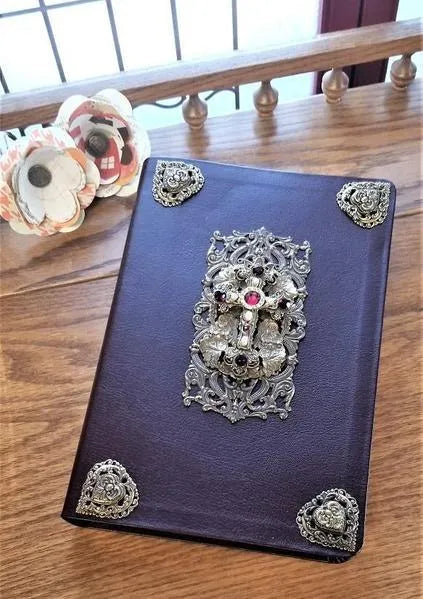 Jeweled Bible with intricate brass accents and gemstone cross on wooden table