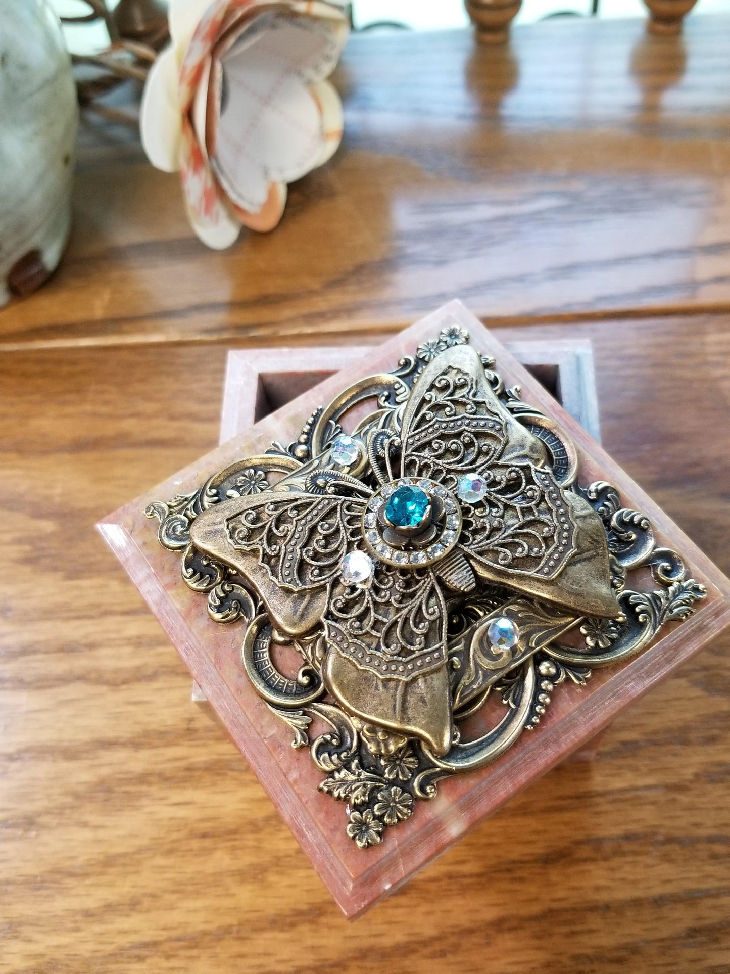Ornate soapstone keepsake box with jeweled butterfly and blue gemstones, open on wood table.