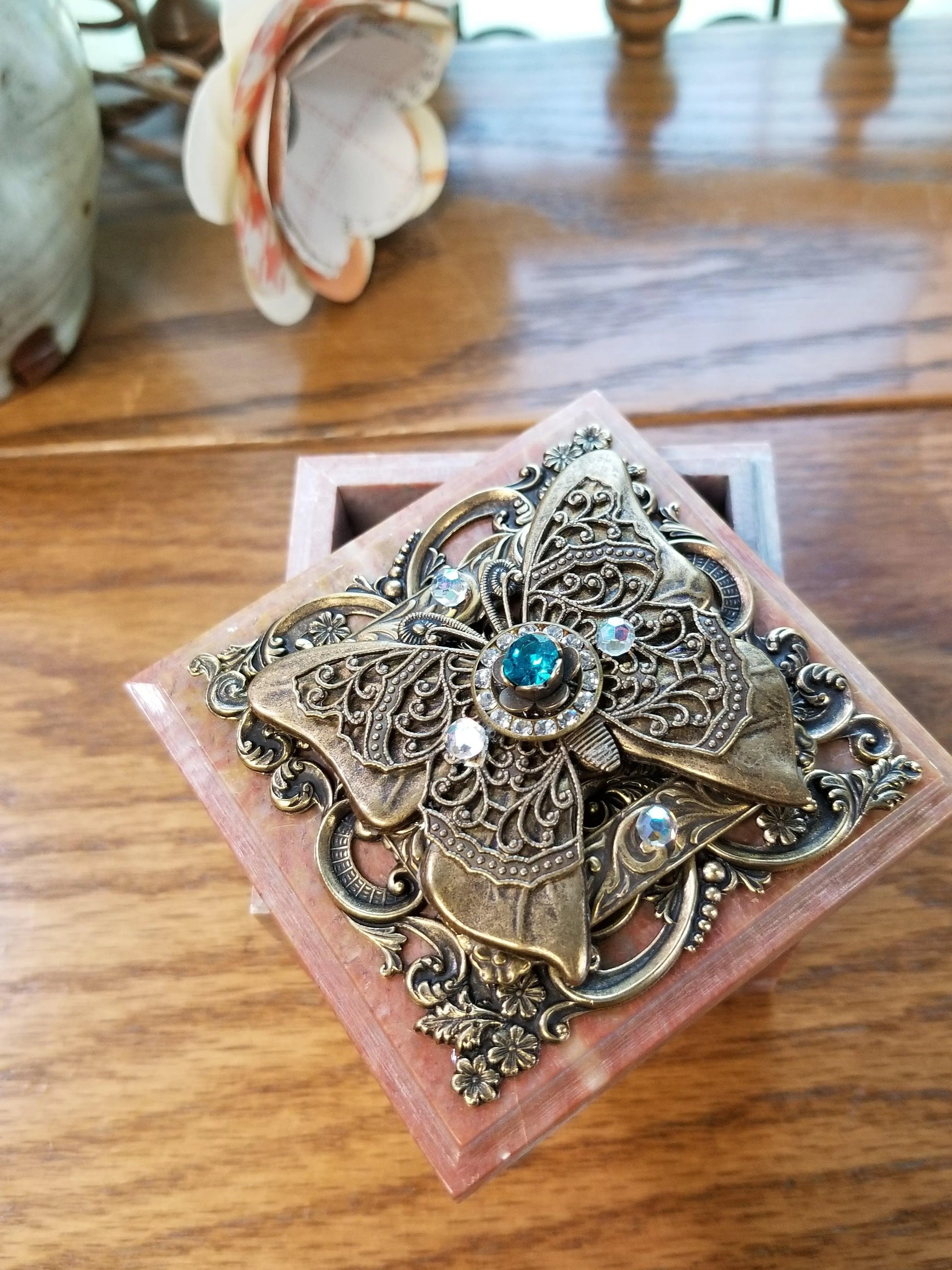 Ornate soapstone keepsake box with jeweled butterfly and blue gemstones, open on wood table.