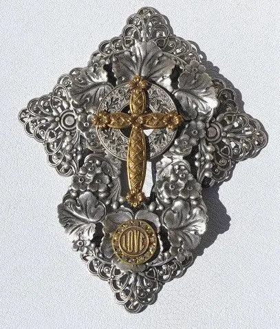 Ornate metal jeweled cross with intricate silver floral design and gold accents, close up