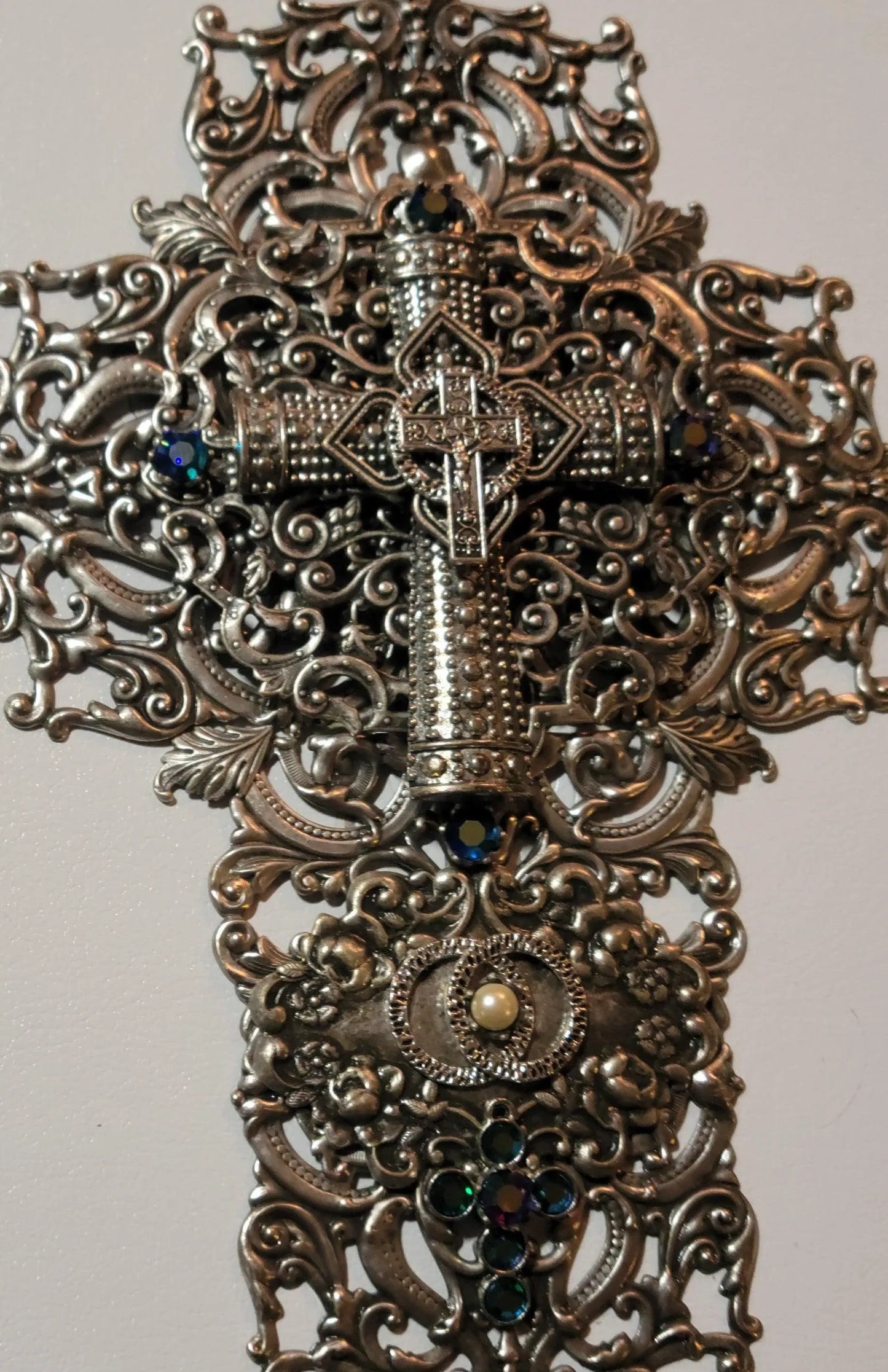 Ornate metal cross with jeweled accents and filigree detail, closeup on white background