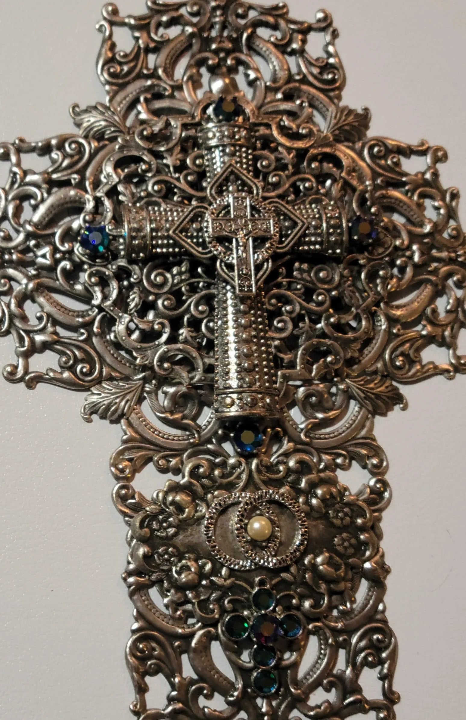 Ornate metal cross with jeweled accents and filigree detail, closeup on white background