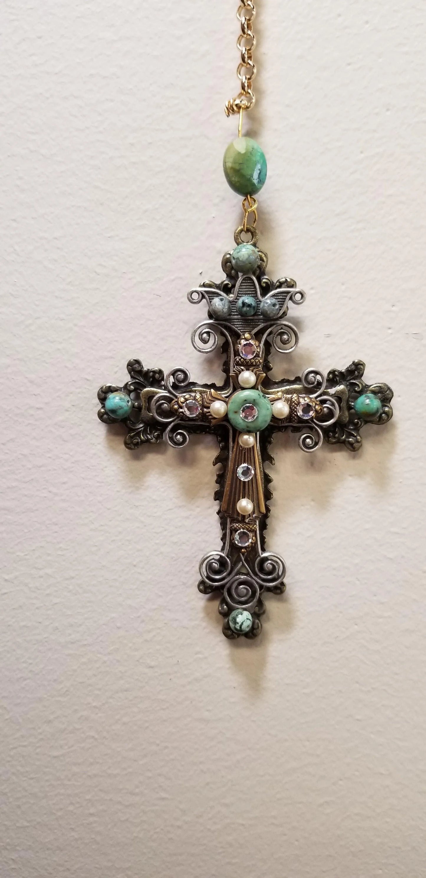 Antique-style jeweled cross ornament with green stones, pearls, and clear gems on gold chain.