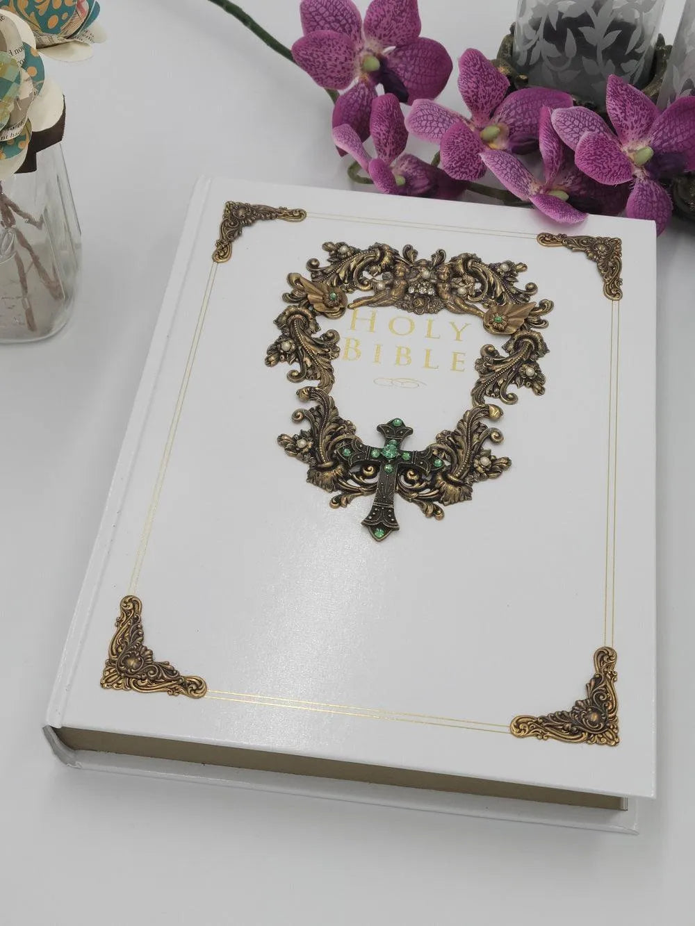 White jeweled family Bible with ornate gold detailing, surrounded by purple flowers