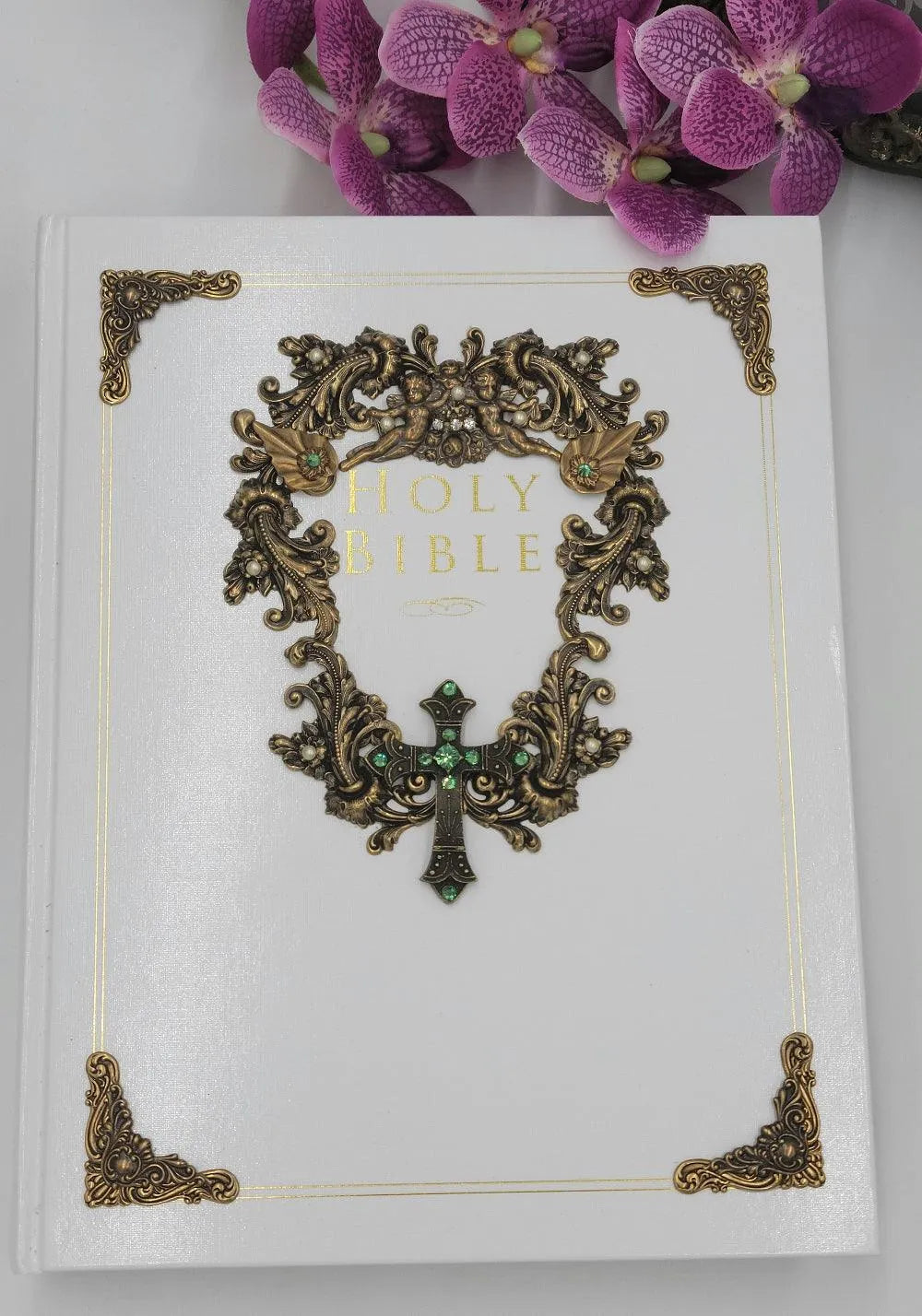 Jeweled white family Bible with ornate gold embellishments and decorative cross, purple flowers nearby.