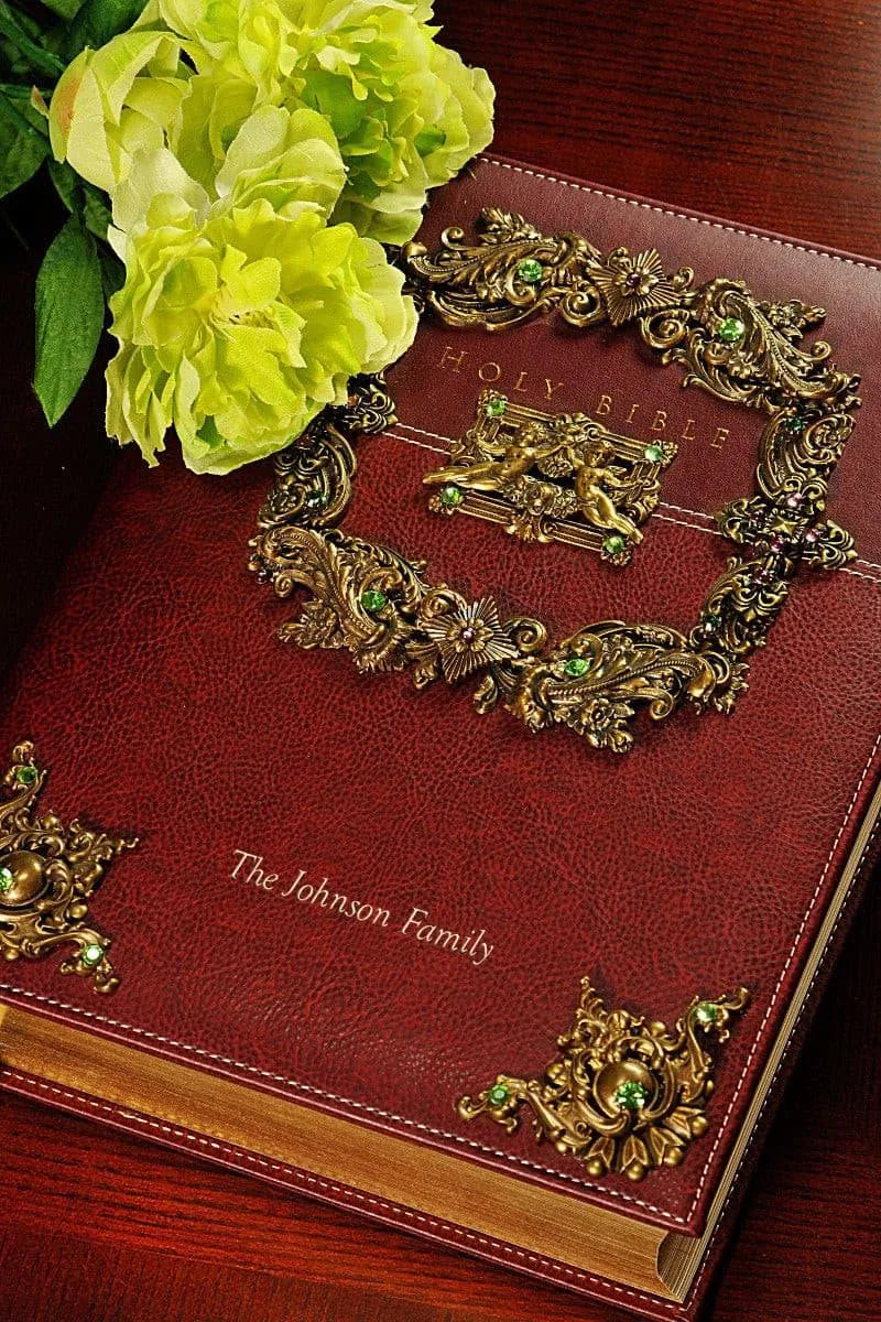 Jeweled family Bible with gold and green ornate metalwork on a red leather cover, beside yellow flowers